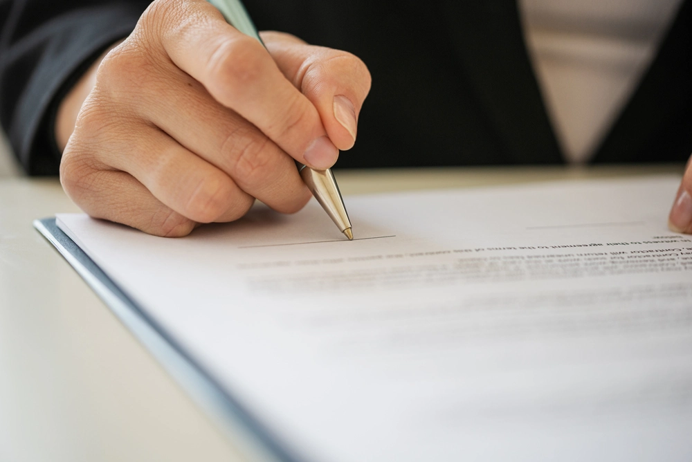Closeup view of hand of a businesswoman or lawyer signing document with a pen.