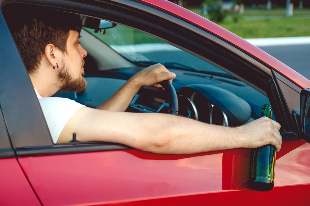 Drunk young man driving a car with a bottle of beer